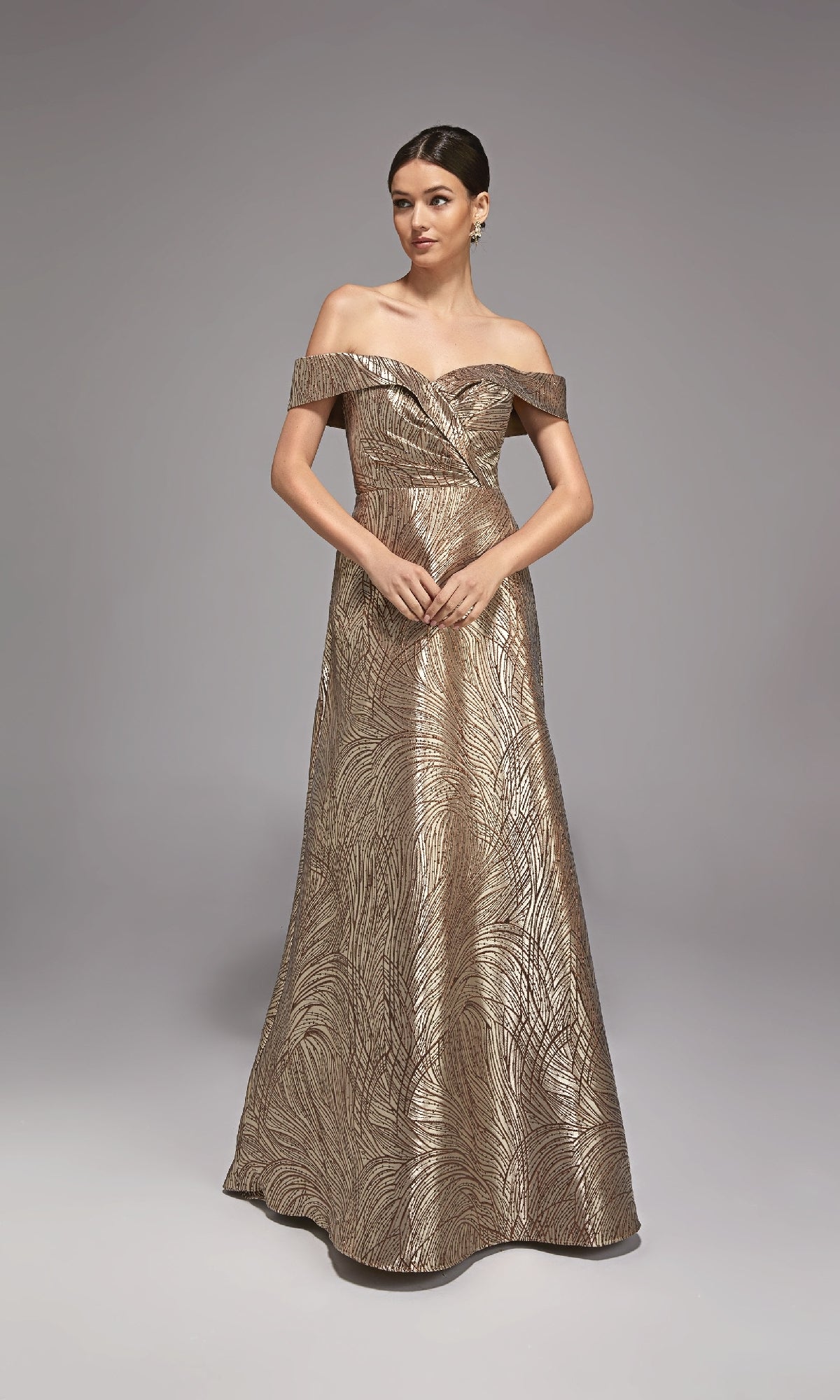 A woman poses against a plain gray background wearing the Alyce 27844 long formal dress in cappuccino, an off-the-shoulder jacquard gown with a leaf-like metallic pattern—ideal as a mother-of-the-bride ensemble.